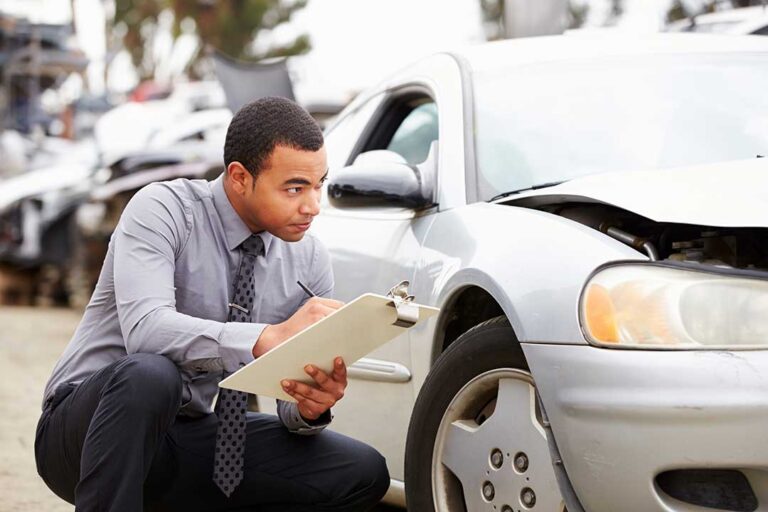 A family reviews insurance documents at a kitchen table beside a home and parked vehicles.